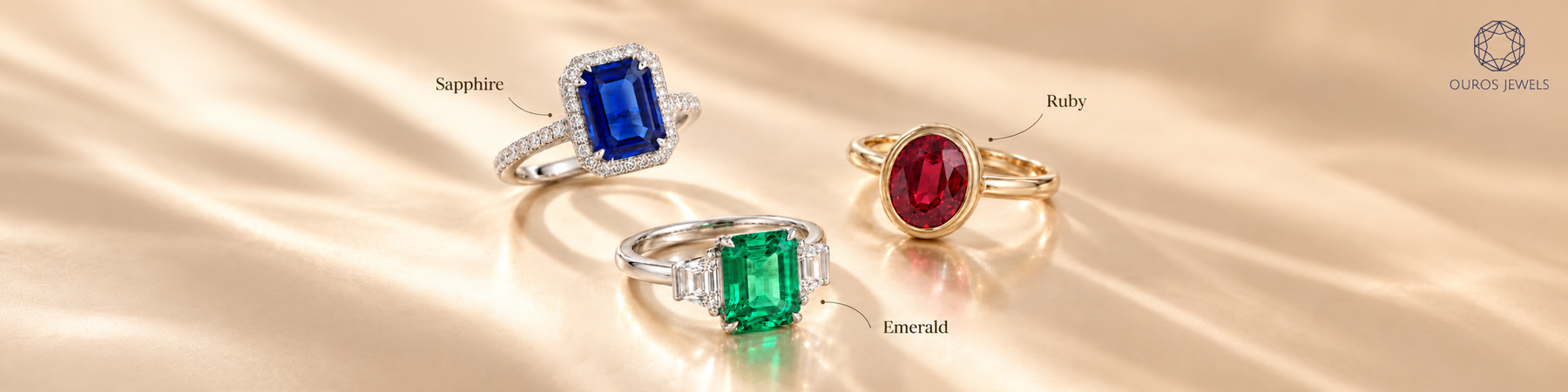 Three gemstone engagement rings: blue sapphire with a halo, oval red ruby in a gold-toned bezel, and green emerald with rectangular side stones.