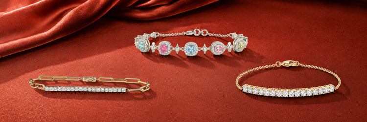 Lab-grown diamond chain bracelets in yellow gold — pavé bar paperclip link bracelet, multi-color fancy cushion cut station bracelet with blue pink and yellow diamonds, and curved round brilliant bar bracelet on red satin