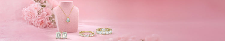 Ouros Jewels Best-selling lab grown diamond Jewelry collection in yellow gold including pear-cut solitaire pendant necklace, emerald-cut stud earrings, marquise and round diamond band, and emerald-cut eternity band on pink velvet display