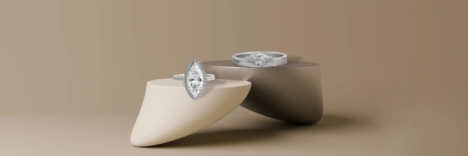 Three marquise cut lab-grown diamond engagement rings in white gold — classic six-prong solitaire, marquise diamond halo with pavé band, and east-west bezel solitaire on taupe pedestals with dappled light
