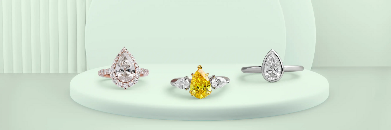 Three pear shaped lab-grown diamond engagement rings in white gold — vintage floral three-stone with marquise and baguette accents, large pear solitaire with pavé band, and pear cut diamond halo ring on cobalt blue display