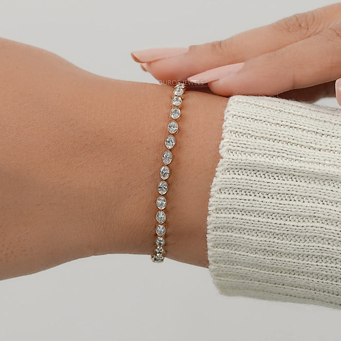 east west set oval cut lab made diamonds bezel set tennis bracelet in yellow gold on hand