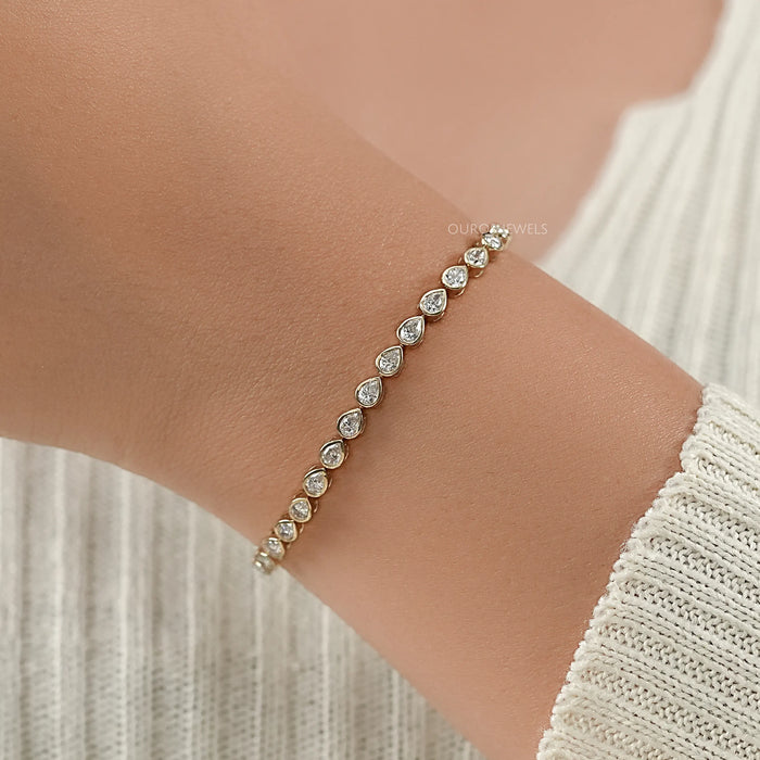 east west set pear cut lab created diamonds bezel set tennis bracelet in yellow gold on hand