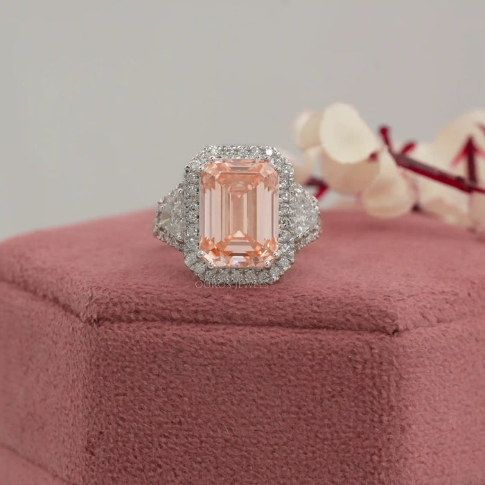 pink emerald cut diamond three stone halo engagement ring on jewelry box