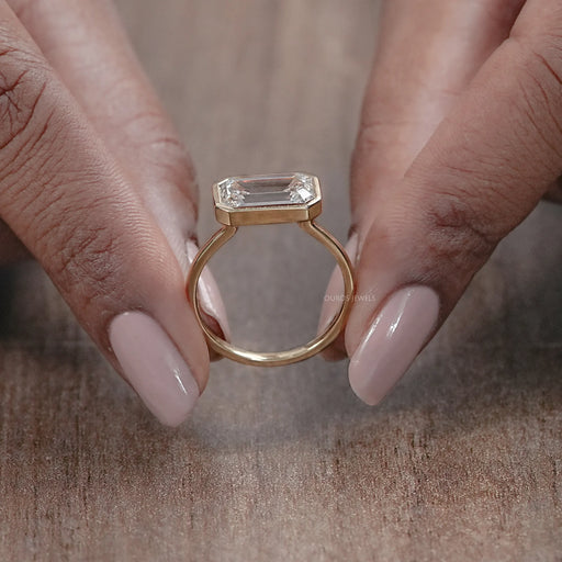 close up view of east west emerald cut lab diamond bezel set engagement ring