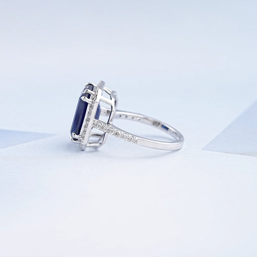 side view of emerald cut sapphire diamond halo ring on sky blue fabric