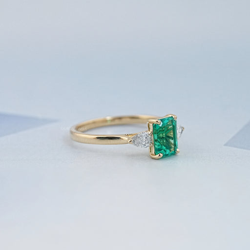 side view of green emerald gemstone and pear diamond three stone engagement ring