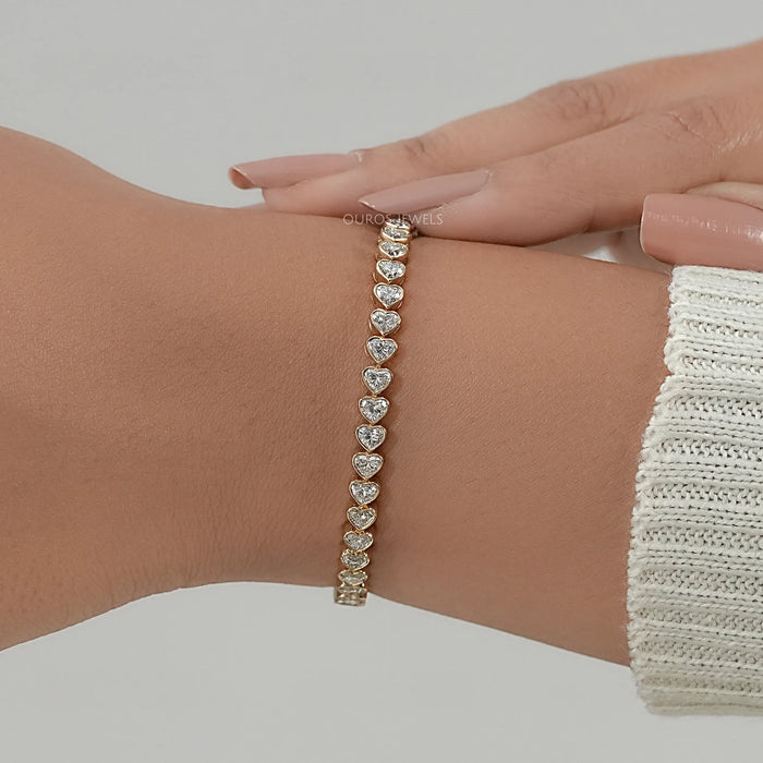 heart cut lab manufatured diamonds bezel set tennis bracelet in yellow gold on hand