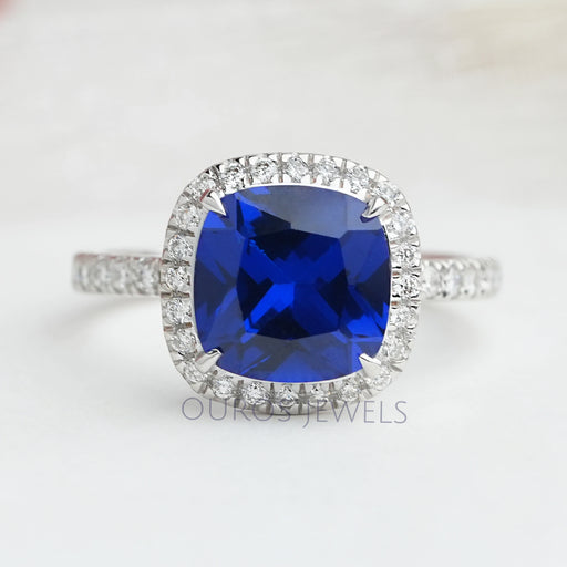 top view of blue cushion cut lab diamond halo engagement ring on grey fabric