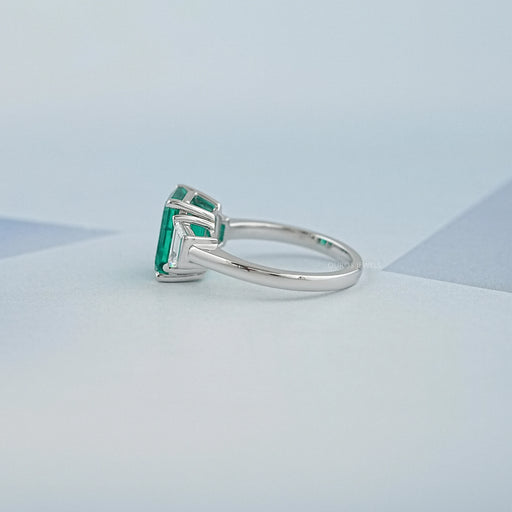 side view of green emerald gemstone with trapezoid diamond 3 stone engagement ring