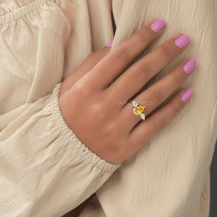 yellow pear cut lab diamond three stone engagement ring in finger